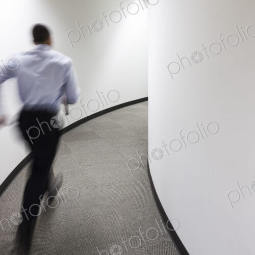 A blur of a businessman running in an office hallway. A blur of a businessman running in an office hallway.