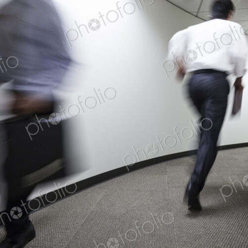 A blur of two businessmen running in an office hallway. A blur of two businessmen running in an office hallway.