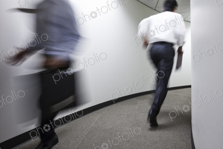 A blur of two businessmen running in an office hallway.