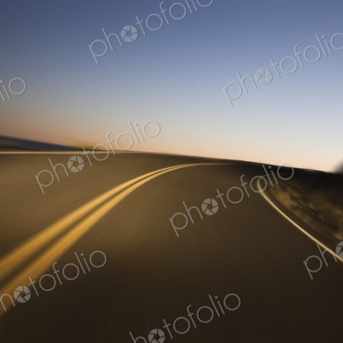 A blurred view of a a road as a car drives on a highway just before sunrise. A blurred view of a a road as a car drives on a highway just before sunrise.