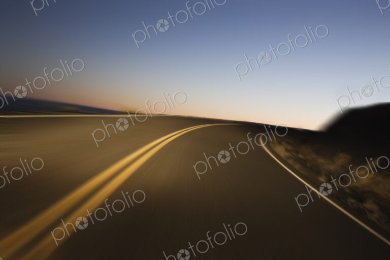 A blurred view of a a road as a car drives on a highway just before sunrise.