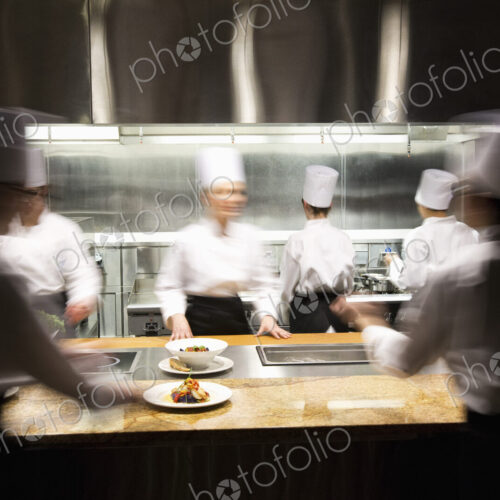 A blurred view of a crew of chefs working around a commercial kitchen. A blurred view of a crew of chefs working around a commercial kitchen.