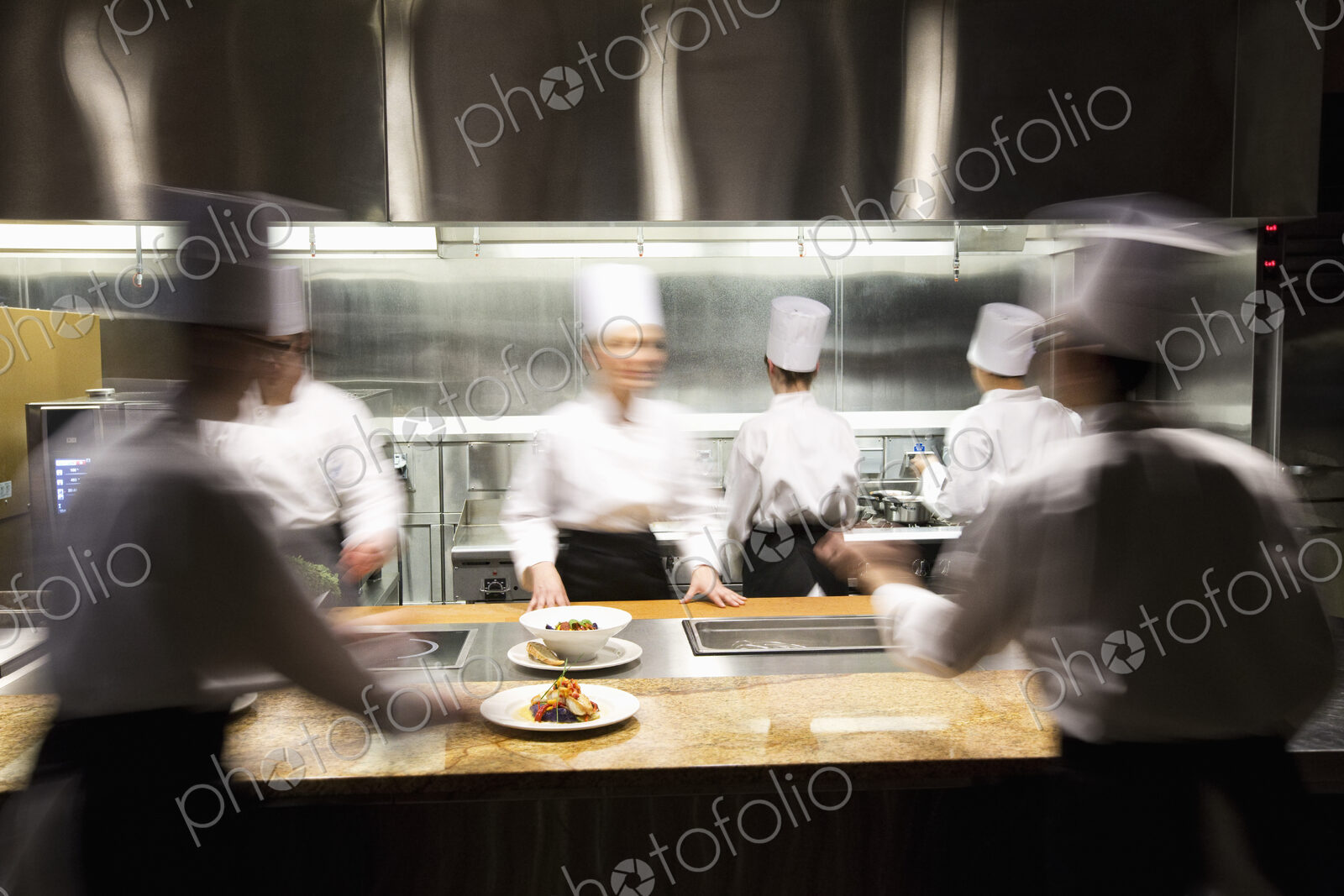 A blurred view of a crew of chefs working around a commercial kitchen.