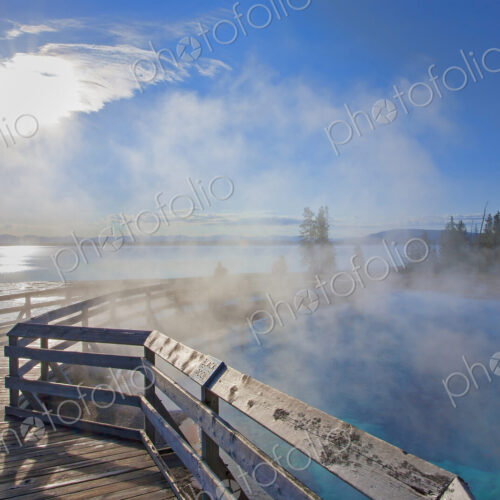 A boardwalk over water, steam rising, people in the background, and view over a lake…