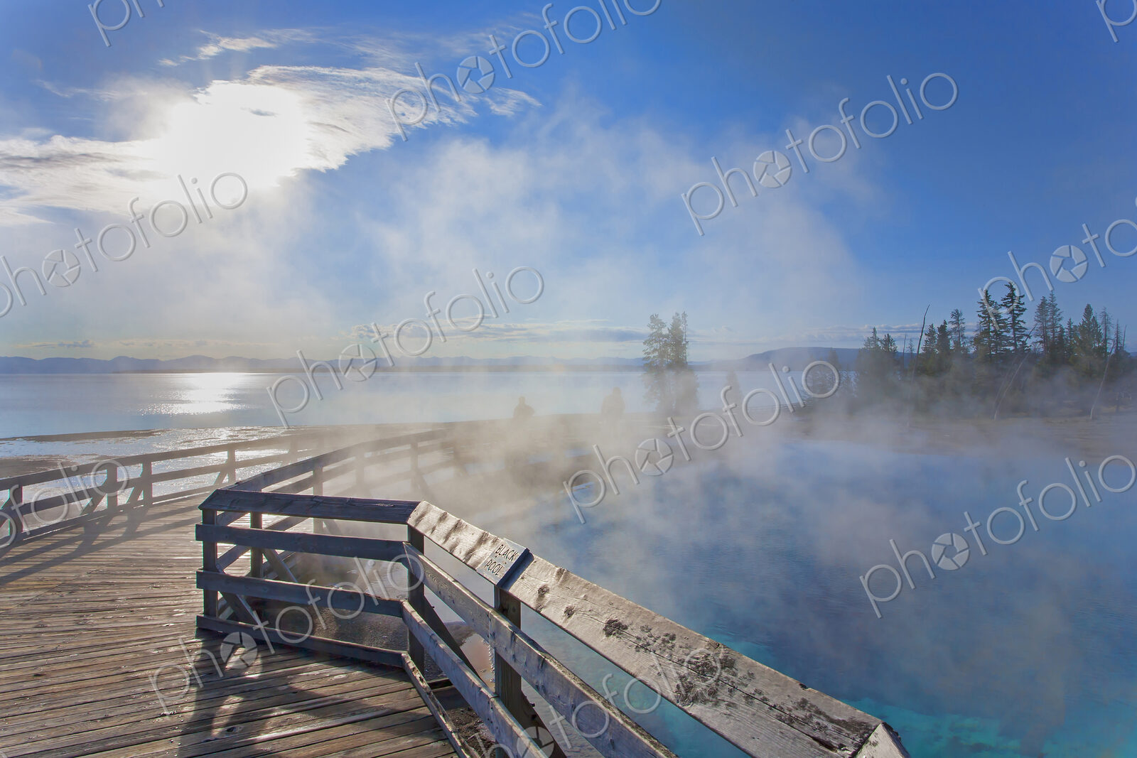 A boardwalk over water, steam rising, people in the background, and view over a lake…