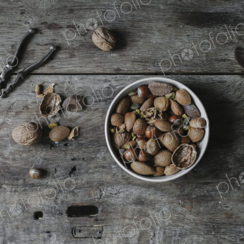 A bowl of mixed nuts, shells nad a nutcracker on a table.
