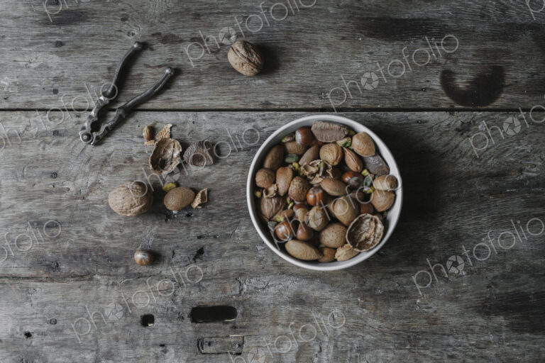 A bowl of mixed nuts, shells nad a nutcracker on a table.