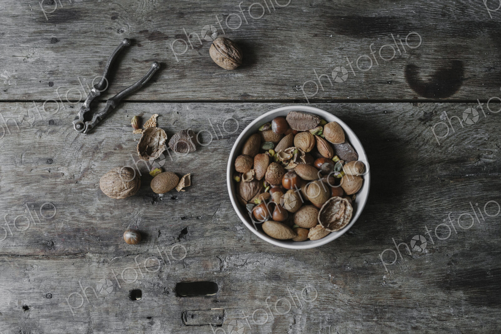 A bowl of mixed nuts, shells nad a nutcracker on a table.