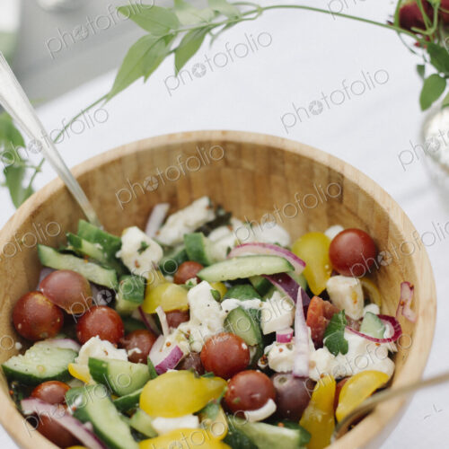 A bowl of salad on a table in a garden of fresh tomatoes, cucumbers and peppers.