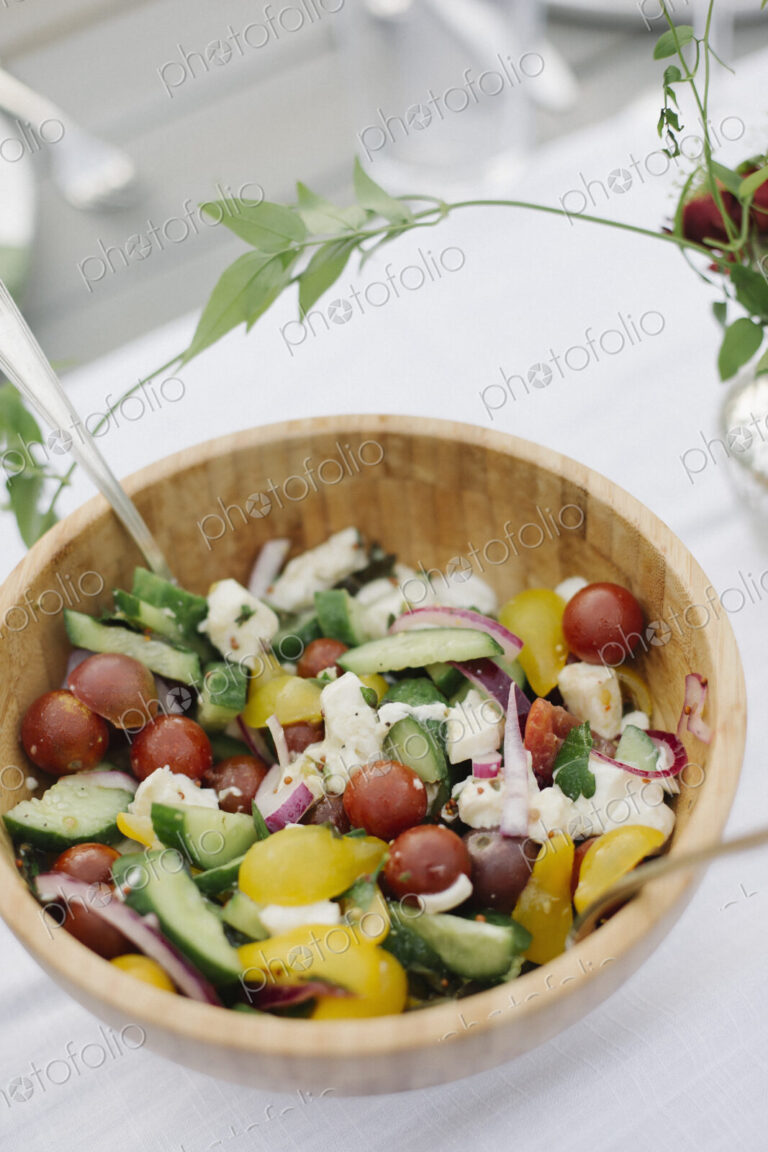 A bowl of salad on a table in a garden of fresh tomatoes, cucumbers and peppers.