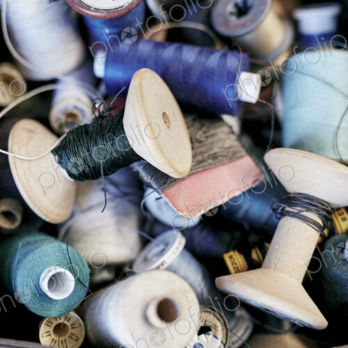A box of coloured sewing threads on wooden and plastic reels.