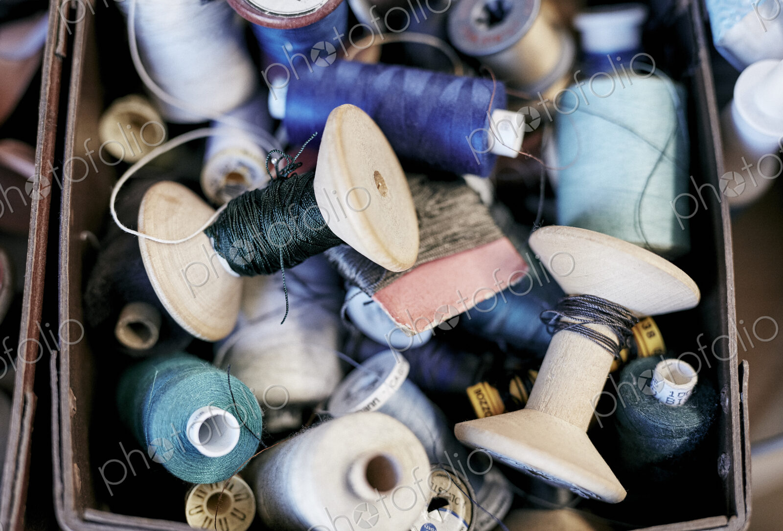 A box of coloured sewing threads on wooden and plastic reels.