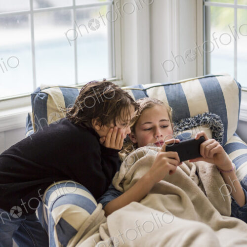 A boy and a teenage girl looking at the screen of a smart phone. A boy and a teenage girl looking at the screen of a smart phone.