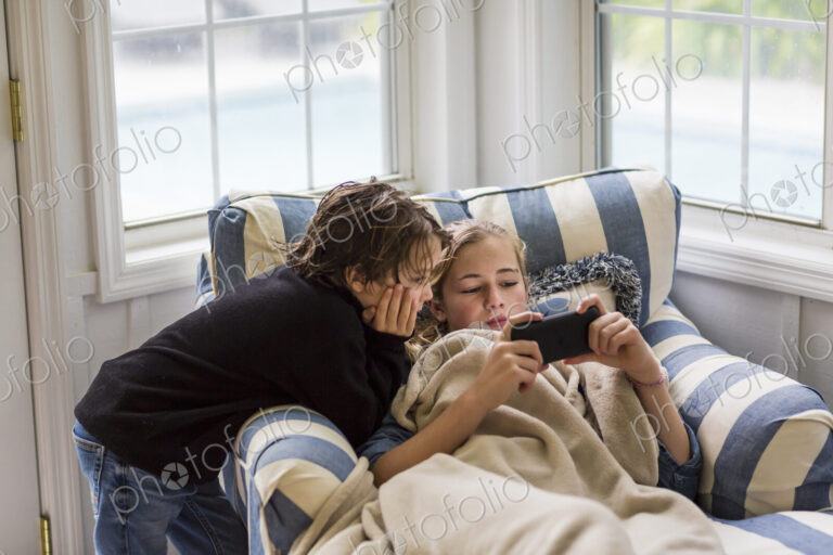 A boy and a teenage girl looking at the screen of a smart phone.