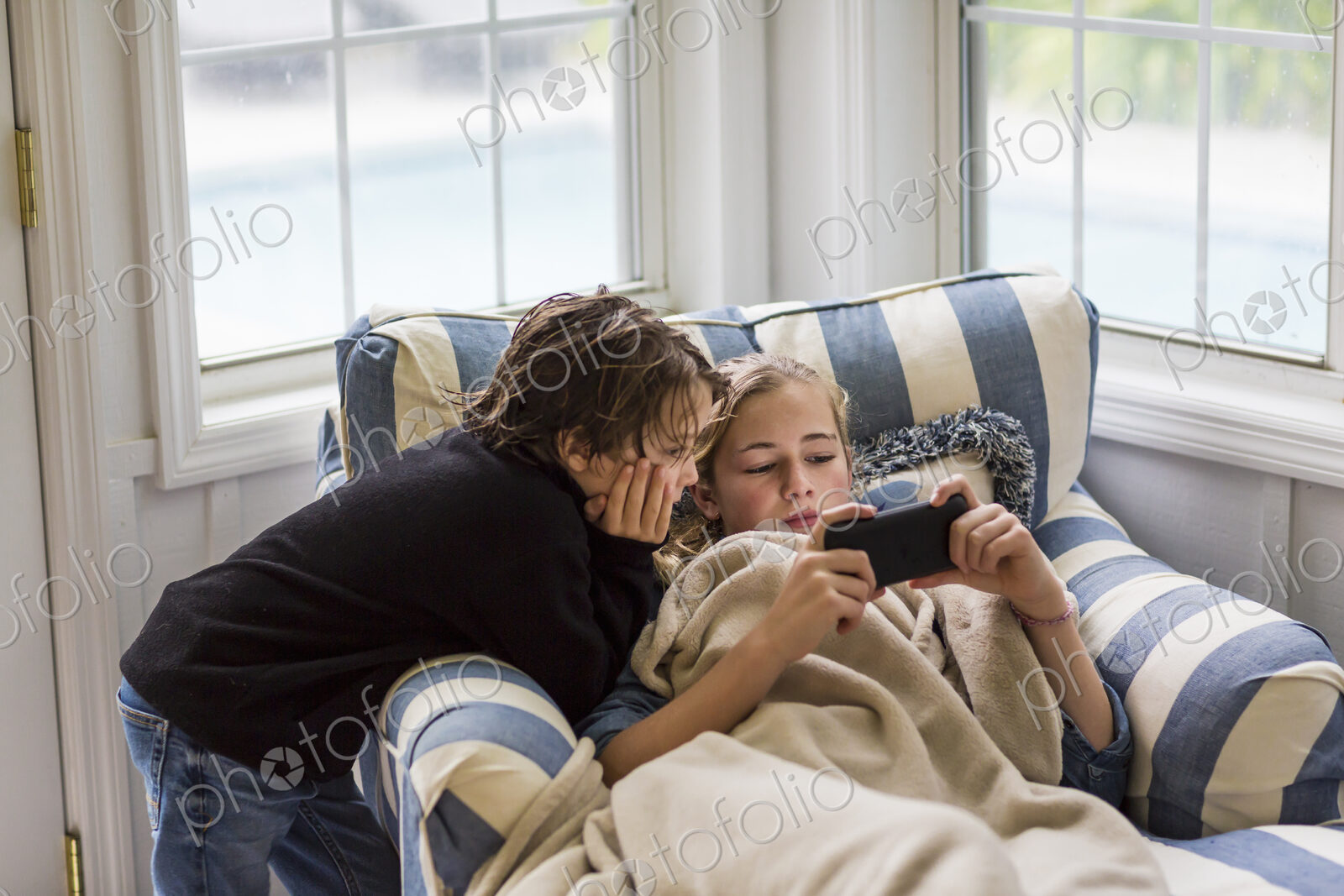 A boy and a teenage girl looking at the screen of a smart phone.