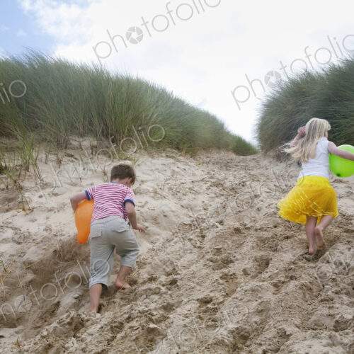 A boy and girl running though soft sand into the sand dunes.