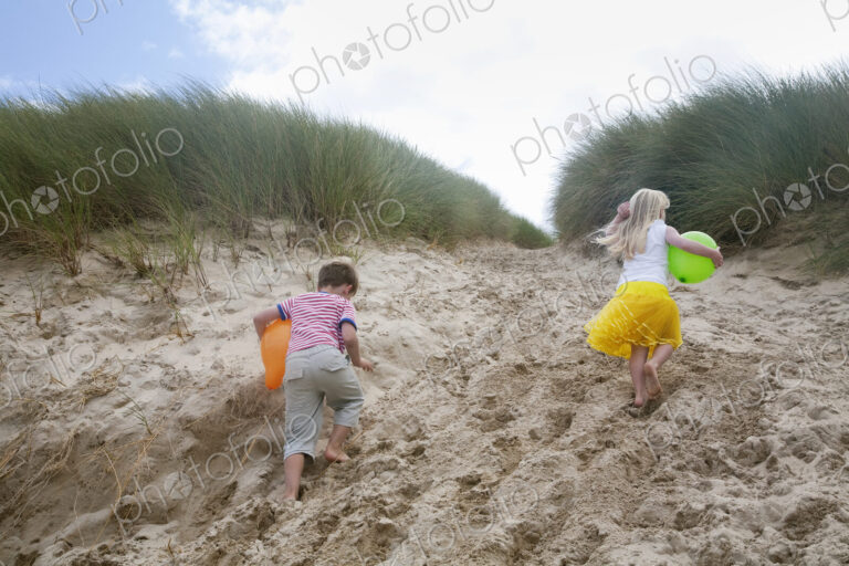 A boy and girl running though soft sand into the sand dunes.