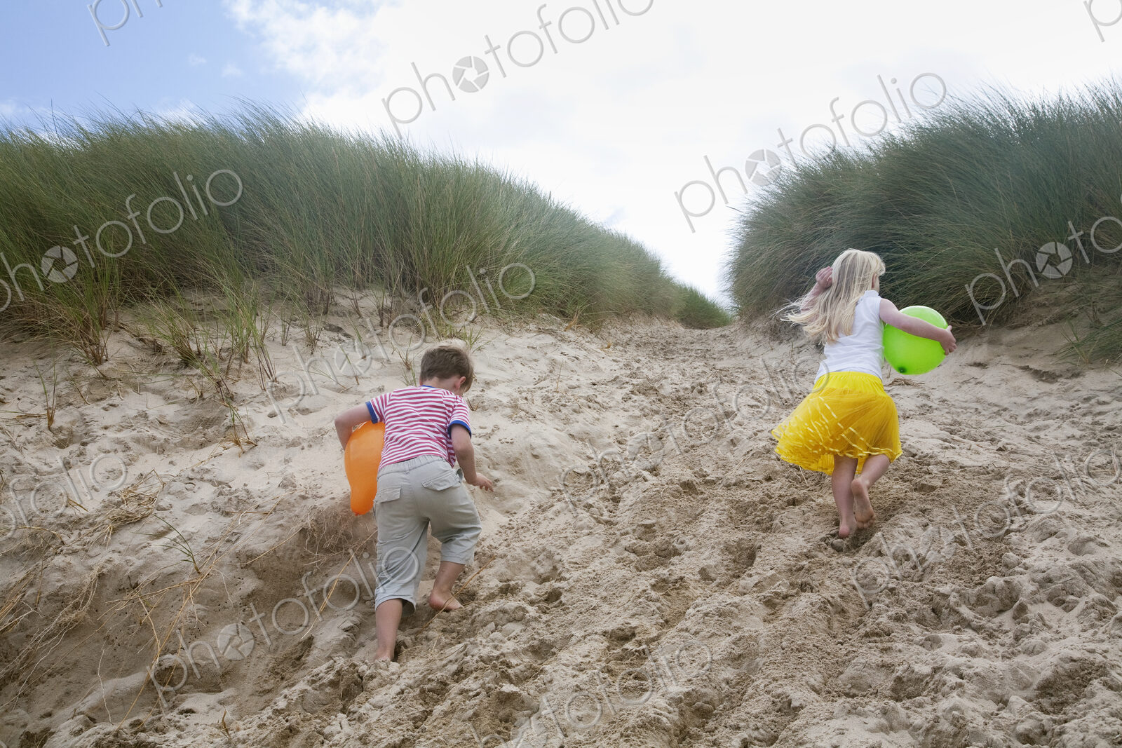 A boy and girl running though soft sand into the sand dunes.