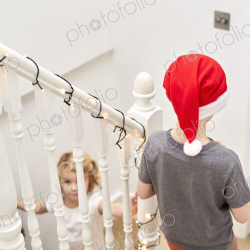 A boy and girl rushing down the stairs on Christmas morning, one wearing a Santa hat.