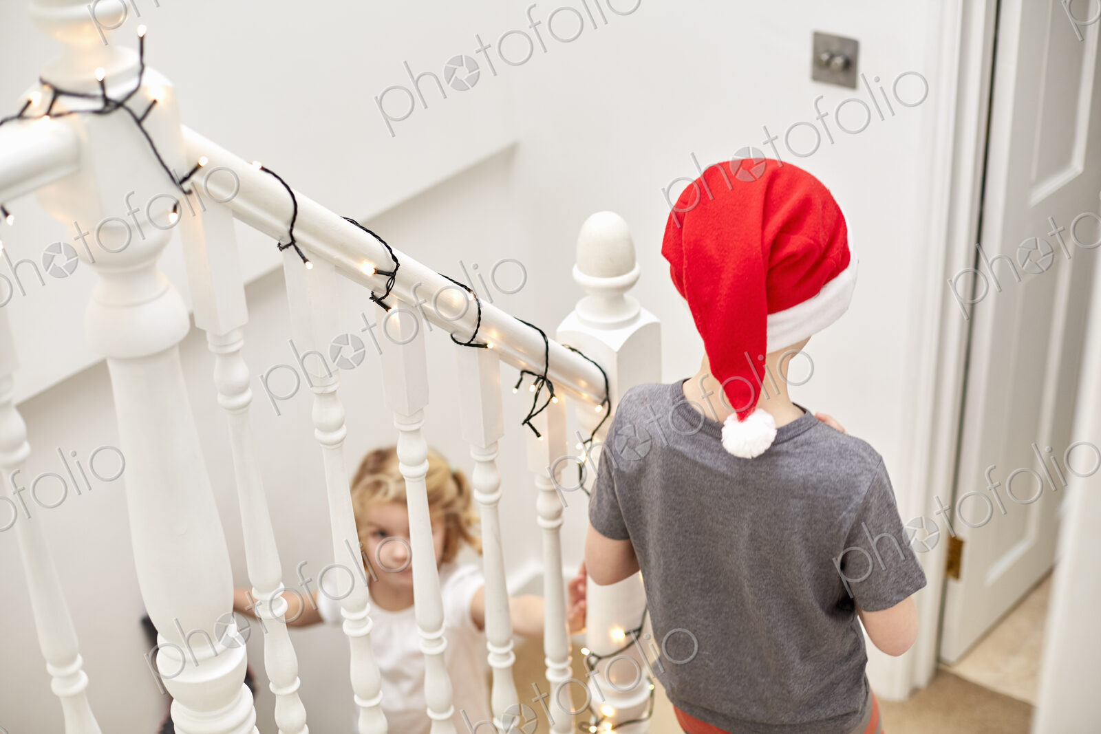 A boy and girl rushing down the stairs on Christmas morning, one wearing a Santa hat.