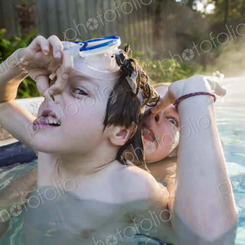 A boy and his sister playing in pool in early morning light, boy holding his nose. A boy and his sister playing in pool in early morning light, boy holding his nose.