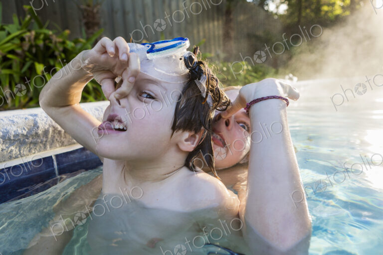 A boy and his sister playing in pool in early morning light, boy holding his nose.