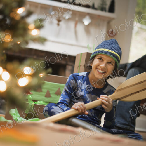 A boy by a Christmas tree unwrapping a gift, a wooden oar.