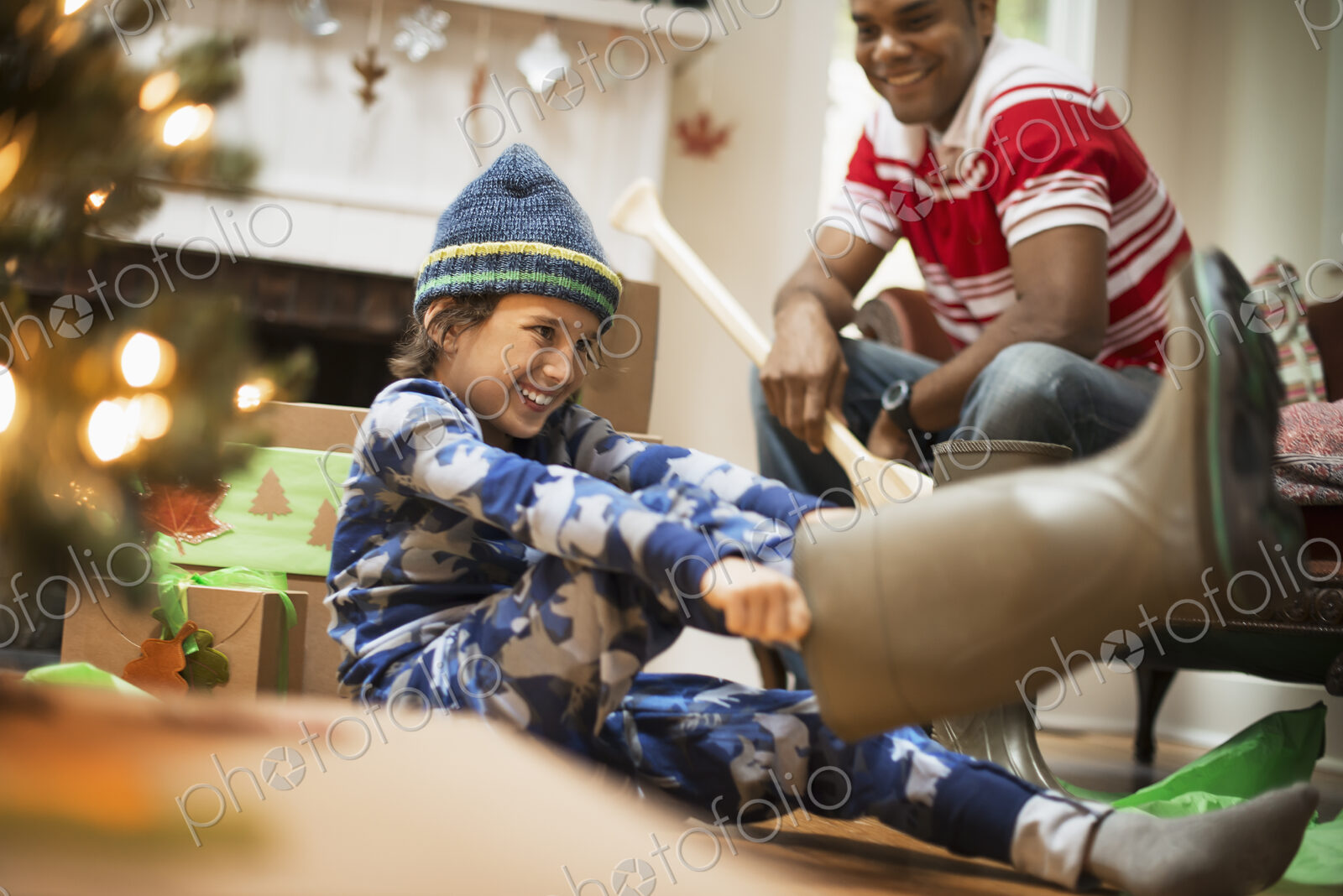 A boy by a Christmas tree unwrapping a gift, and trying on muck boots.