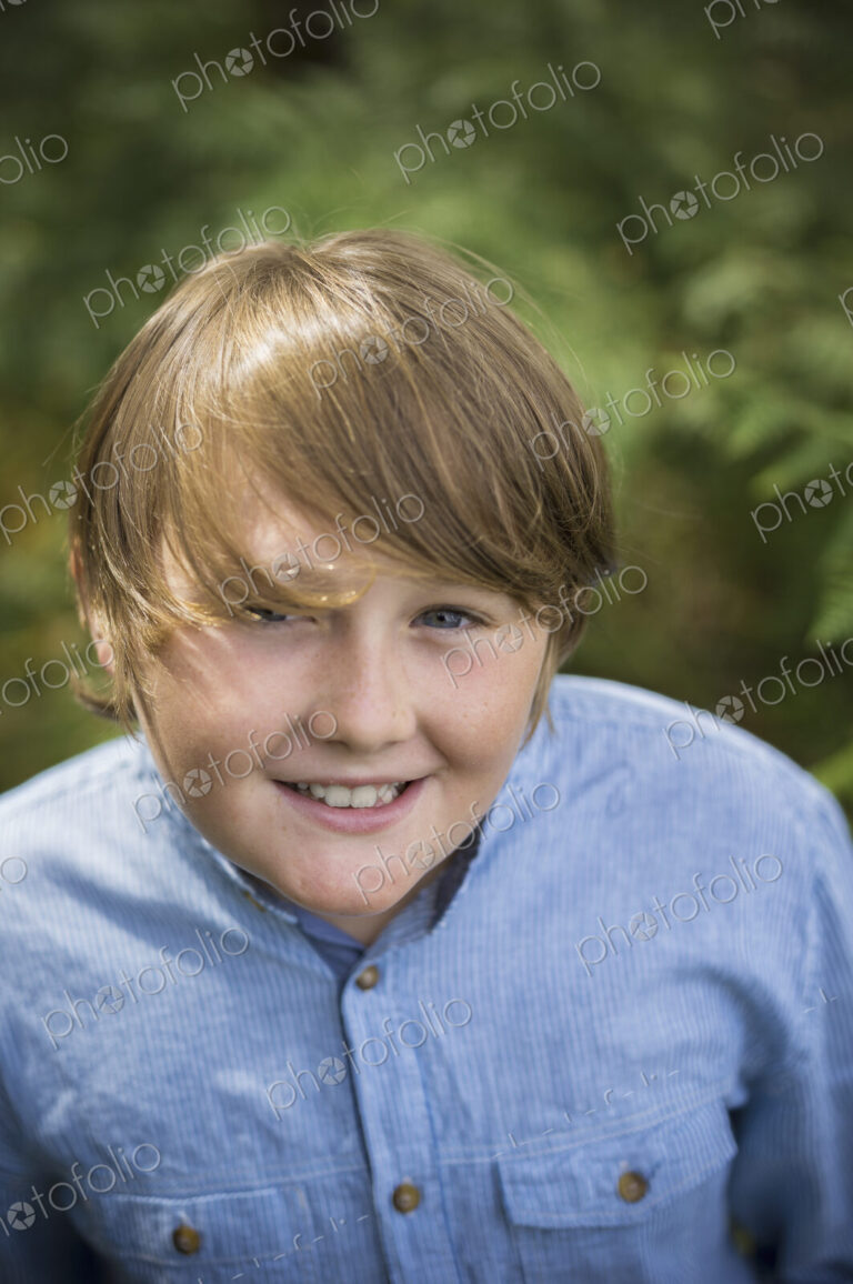 A boy in a denim button down shirt looking up at the camera.