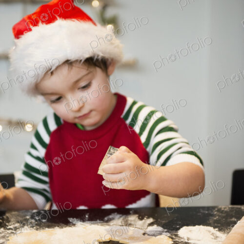 A boy in a santa hat making Christmas biscuits, cutting out shapes.