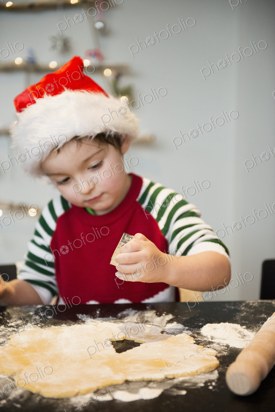 A boy in a santa hat making Christmas biscuits, cutting out shapes.