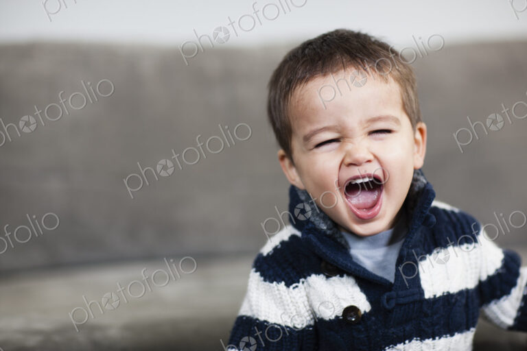 A boy in a striped shirt opening his mouth wide.