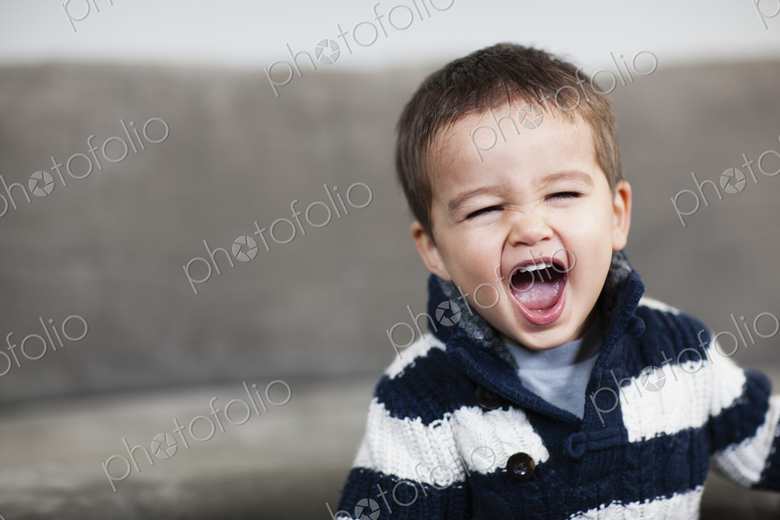 A boy in a striped shirt opening his mouth wide.