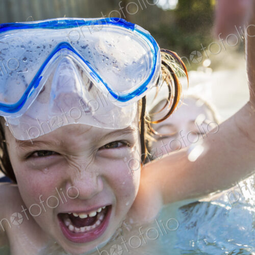 A boy in goggles laughing at the camera, in a warm swimming pool with his sister. A boy in goggles laughing at the camera, in a warm swimming pool with his sister.