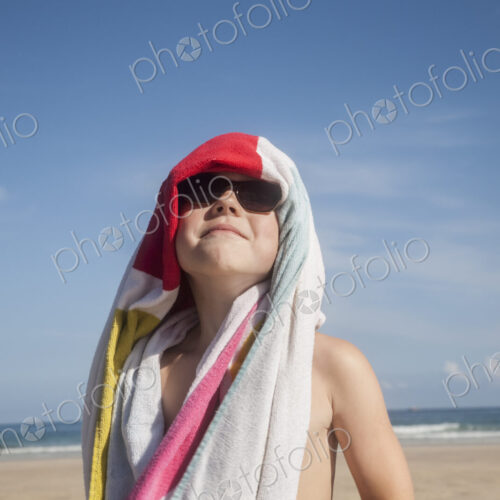 A boy in sunglasses with a towel over his head.