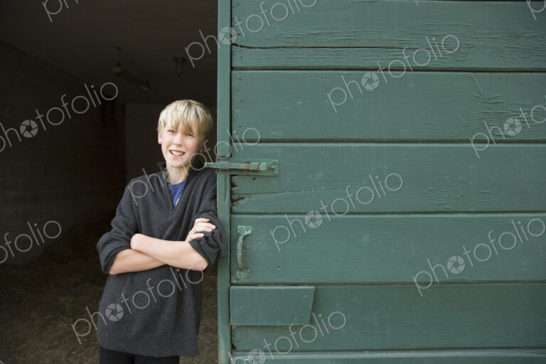 A boy leaning against a wooden barn door, at an animal sanctuary.