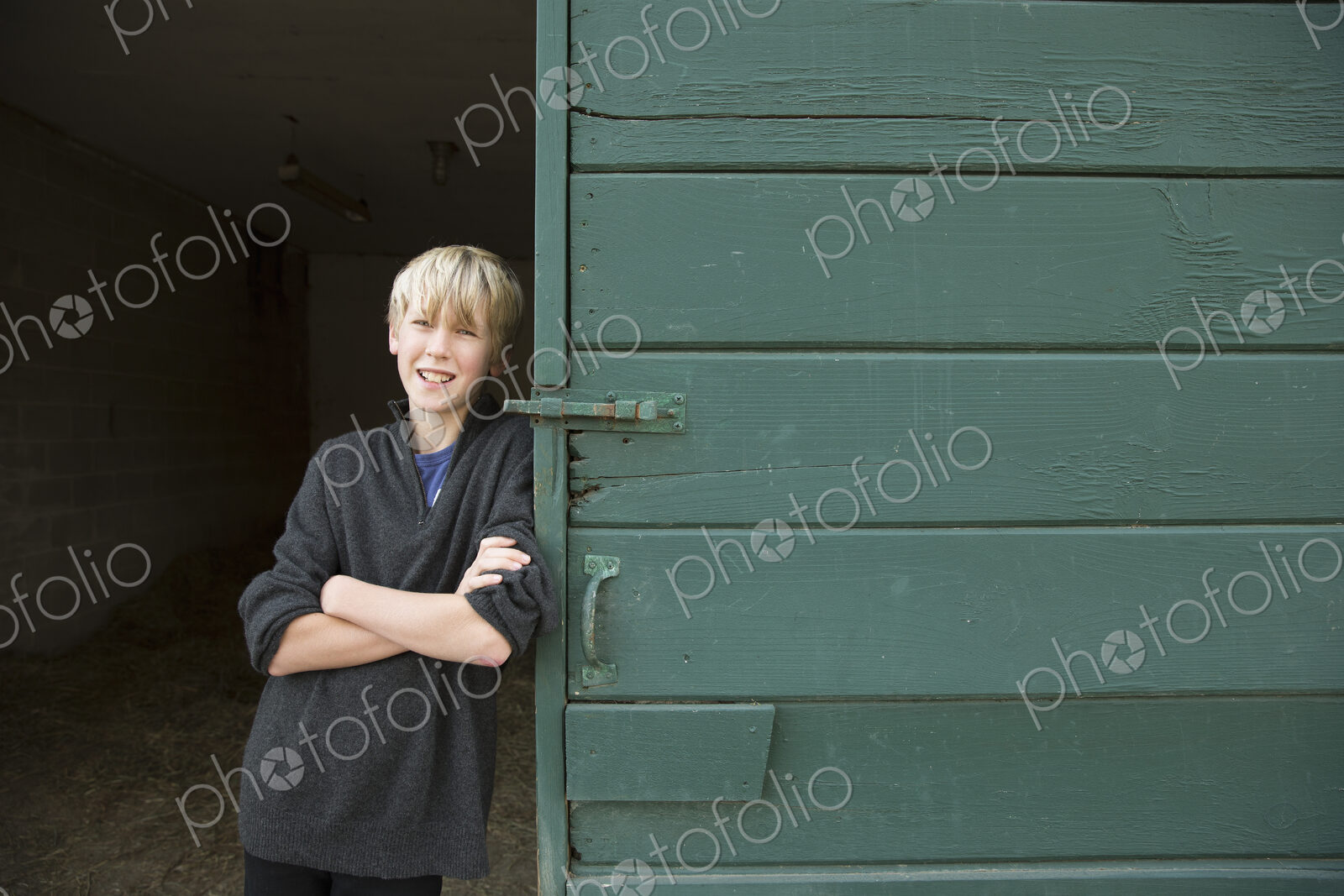 A boy leaning against a wooden barn door, at an animal sanctuary.