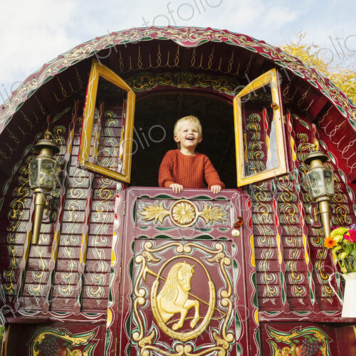 A boy leaning out of the open shutters at the rear of a bow top gypsy caravan. A boy leaning out of the open shutters at the rear of a bow top gypsy caravan.