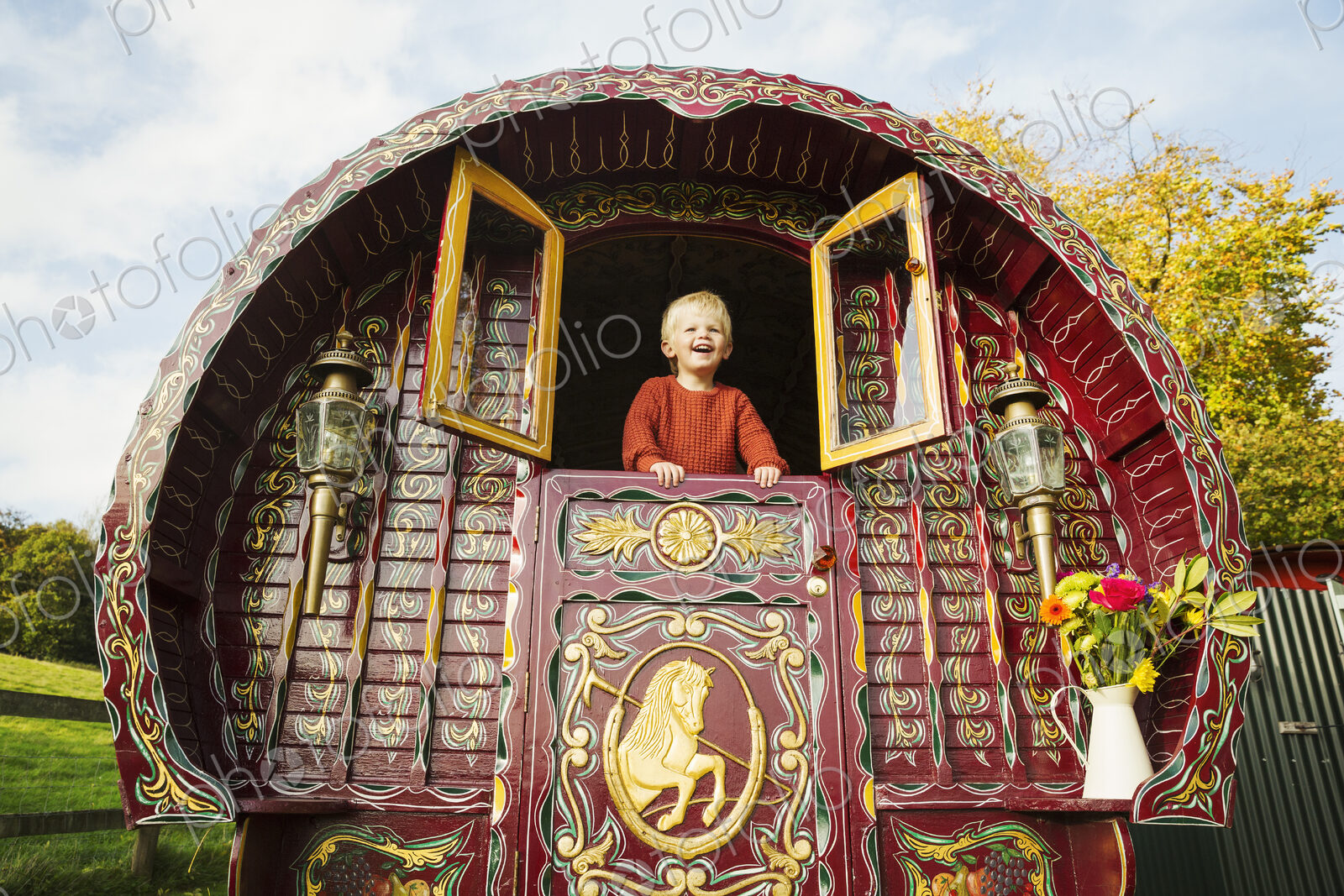A boy leaning out of the open shutters at the rear of a bow top gypsy caravan.