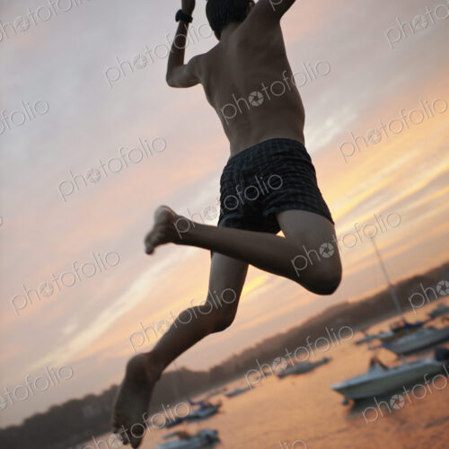 A boy leaping off the dock into the water, at sunset on the coast. A boy leaping off the dock into the water, at sunset on the coast.