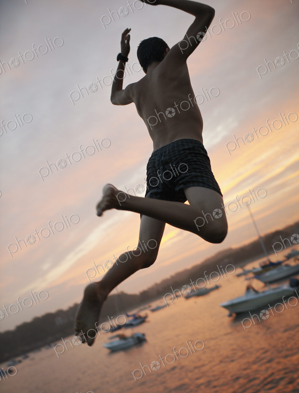 A boy leaping off the dock into the water, at sunset on the coast.