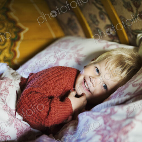 A boy lying in bed under a curved bow top roof of a gypsy caravan, looking at the camera. A boy lying in bed under a curved bow top roof of a gypsy caravan, looking at the camera.