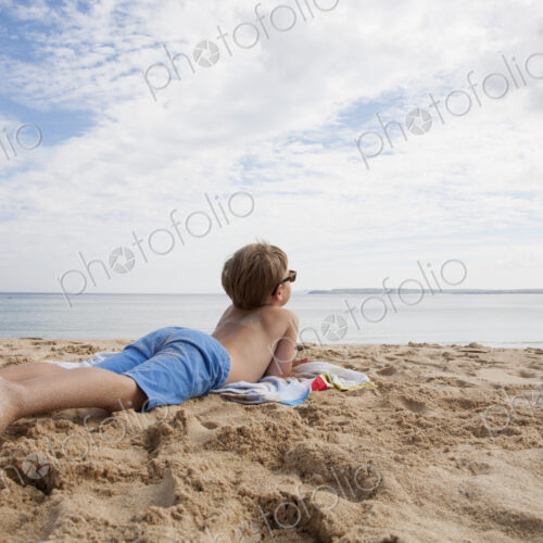 A boy lying on his front on the sand looking out to sea. A boy lying on his front on the sand looking out to sea.