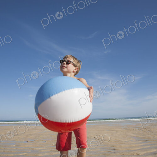 A boy on the beach holding a large inflatable beach ball.
