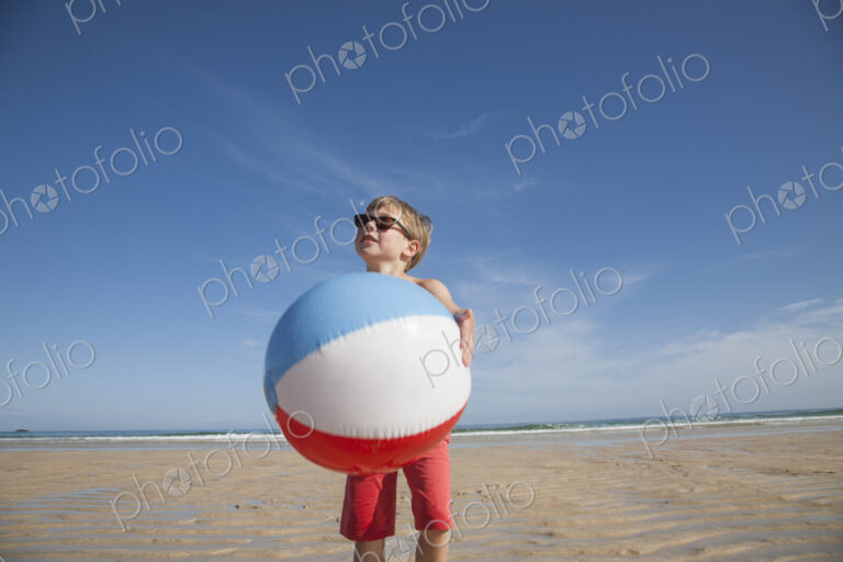 A boy on the beach holding a large inflatable beach ball.