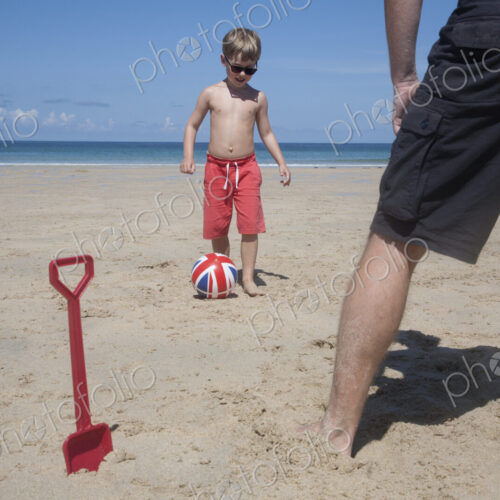 A boy playing football with a man on the sand. Father and son. A beach spade upright… A boy playing football with a man on the sand. Father and son. A beach spade upright…