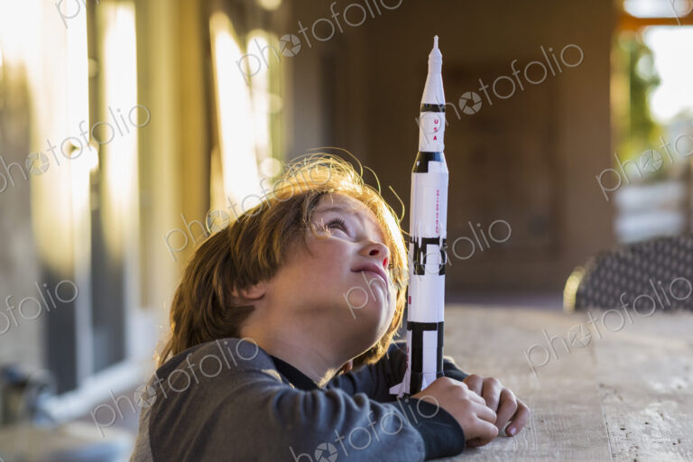A boy playing with a toy Nasa Saturn 5 rocket, day dreaming about space flight.