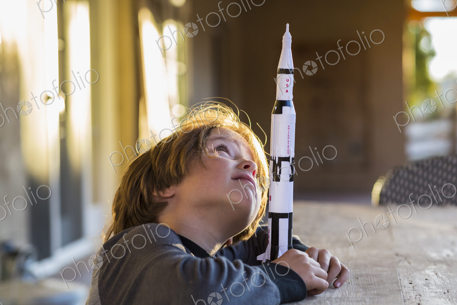 A boy playing with a toy Nasa Saturn 5 rocket, day dreaming about space flight.