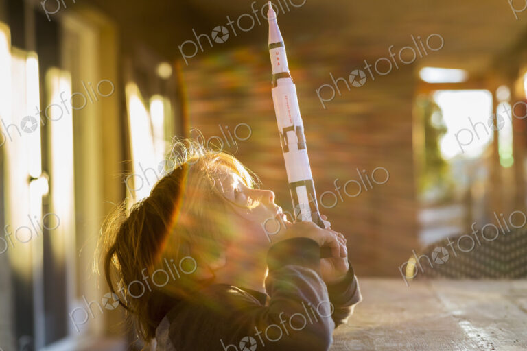 A boy playing with a toy Nasa Saturn 5 rocket, day dreaming about space flight.