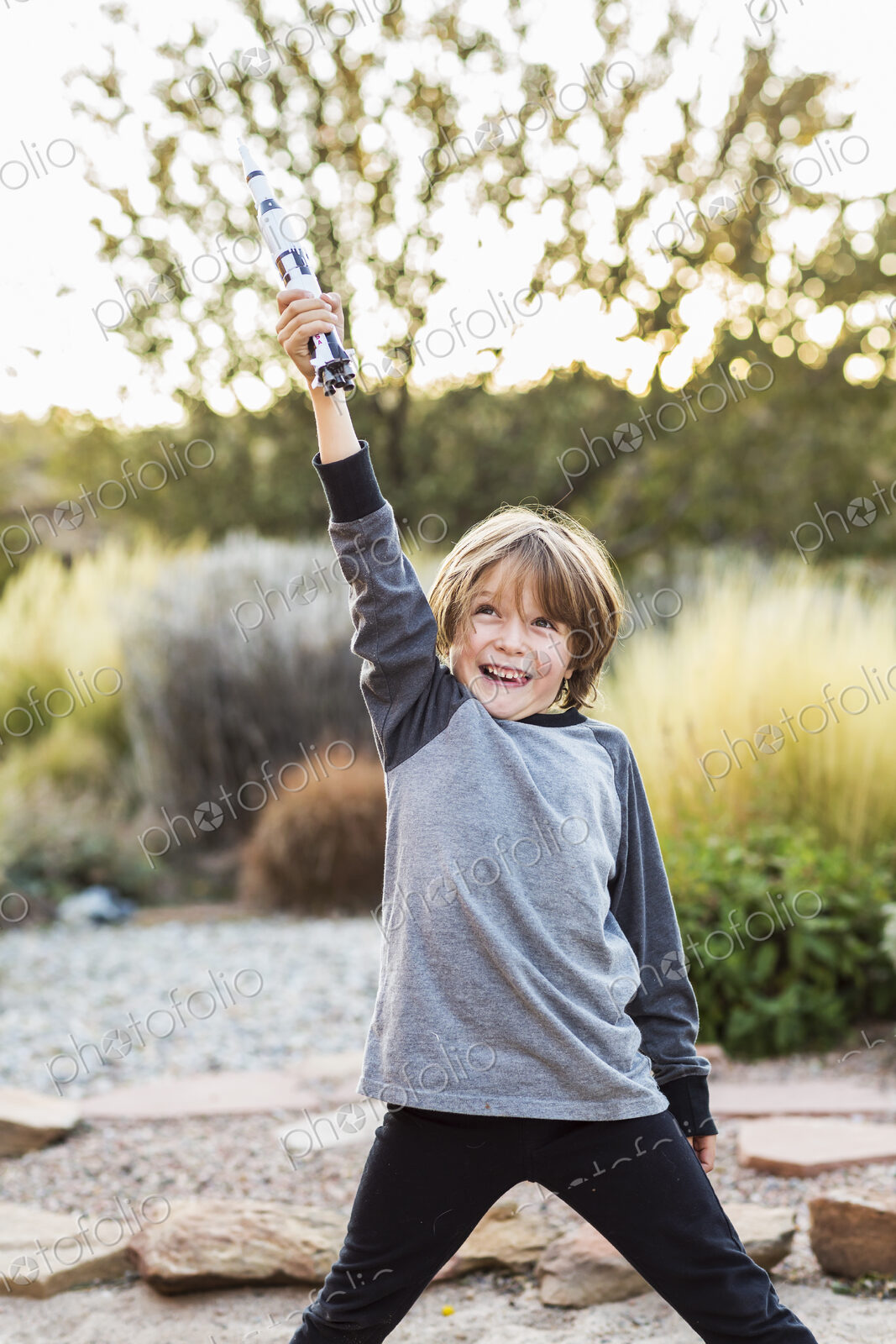 A boy playing with a toy Nasa Saturn 5 rocket, holding it above his head.